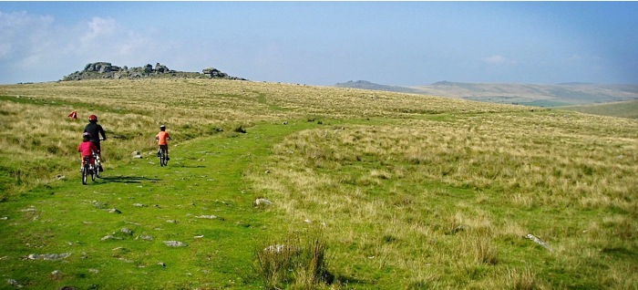 Family cycling on grassy hilltop Dartmoor